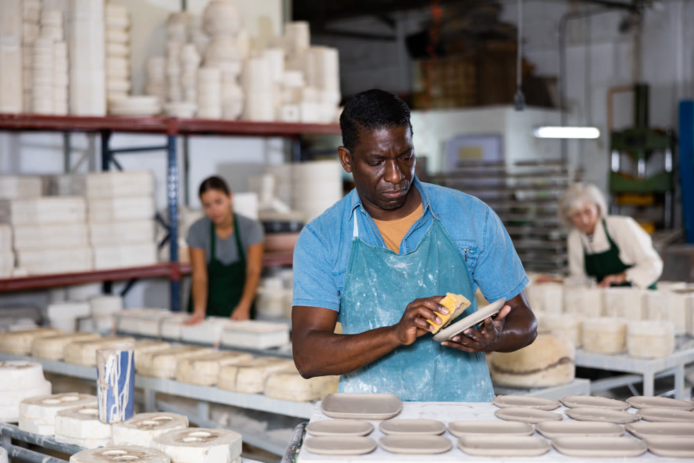African american man prepares pottery with foam sponge - removes roughness and unevenness