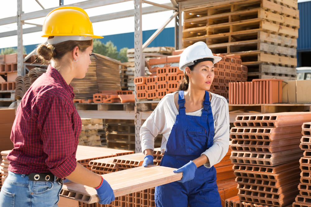 Women carrying flat hollow clay brick in outdoor warehouse