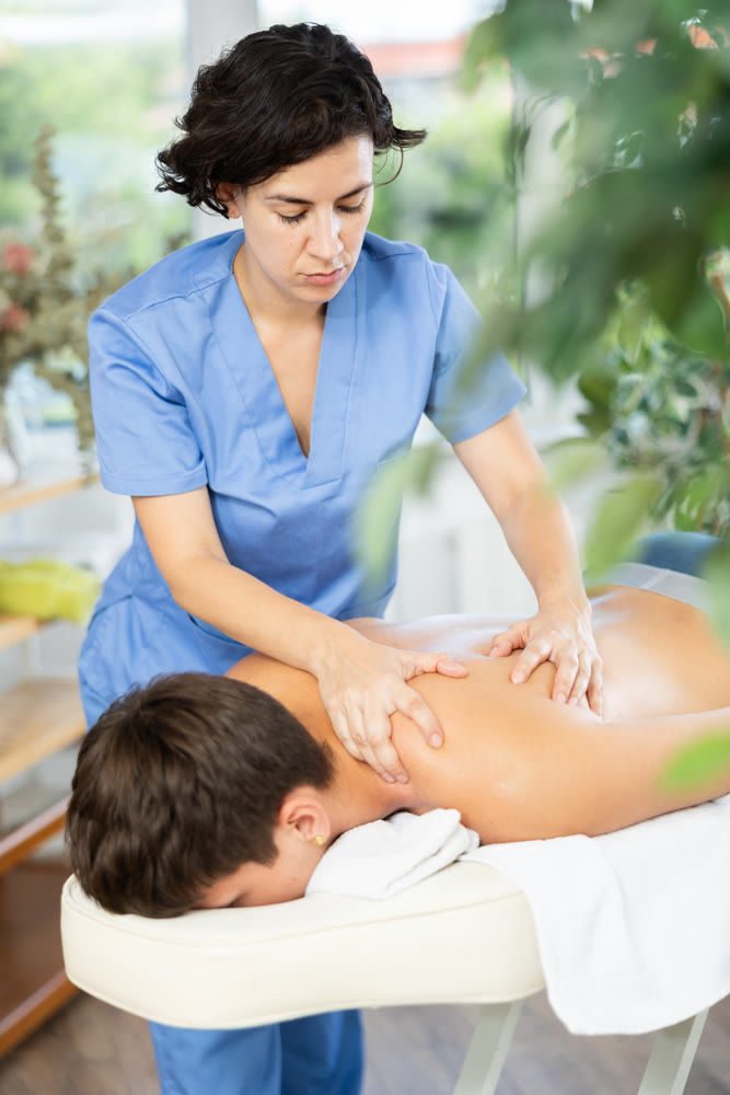 Diligent woman massage therapist massaging relaxing guy at spa complex