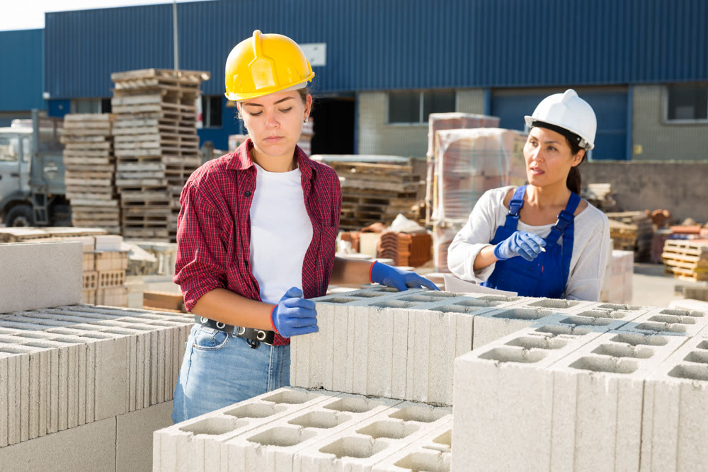 Female builders with hollow concrete blocks in outdoor warehouse