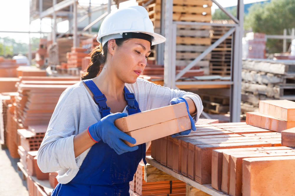 Asian worker stacking bricks in warehouse of building materials on an open-air site