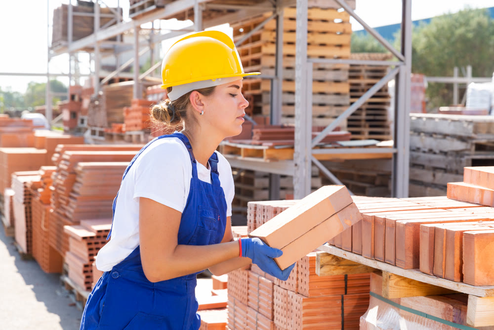 Worker stacking bricks in warehouse of building materials on an open-air site
