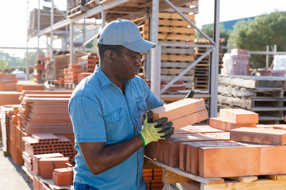 Male builder carrying bricks in outdoor warehouse