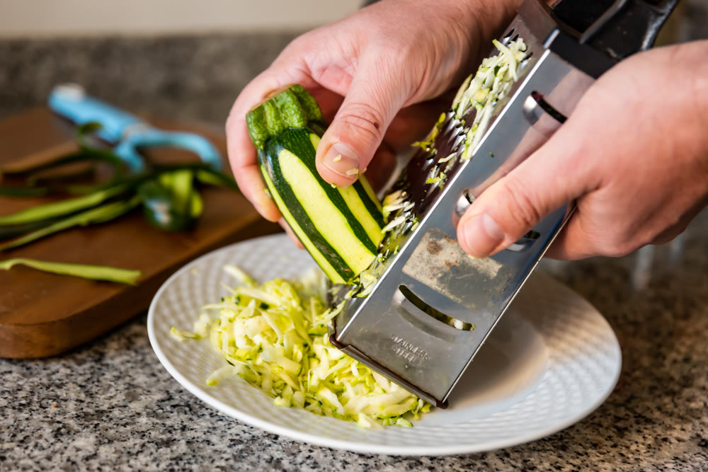 Hands rubs zucchini on grater close-up