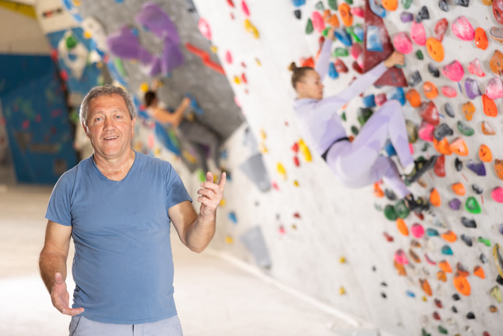 Positive aged man inviting to workout in climbing center
