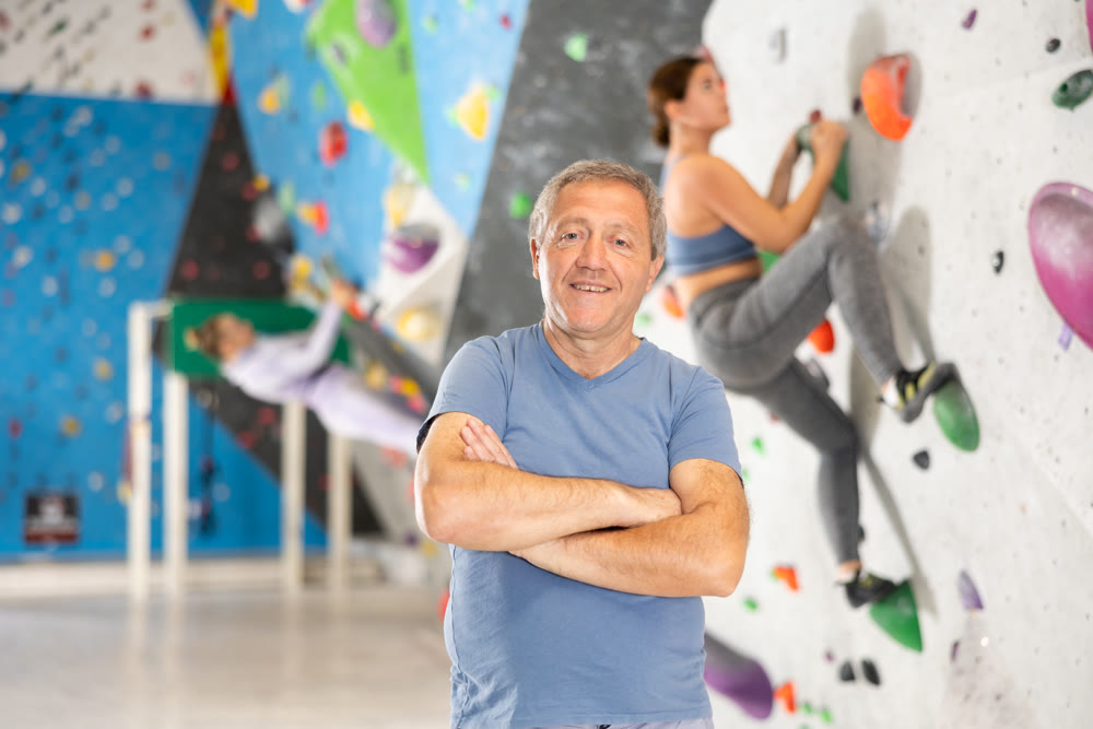 Positive senior coach man on the background of climbing wall