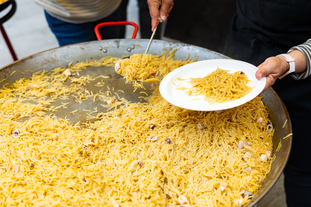 Chef serving seafood fideua into plates at street festival