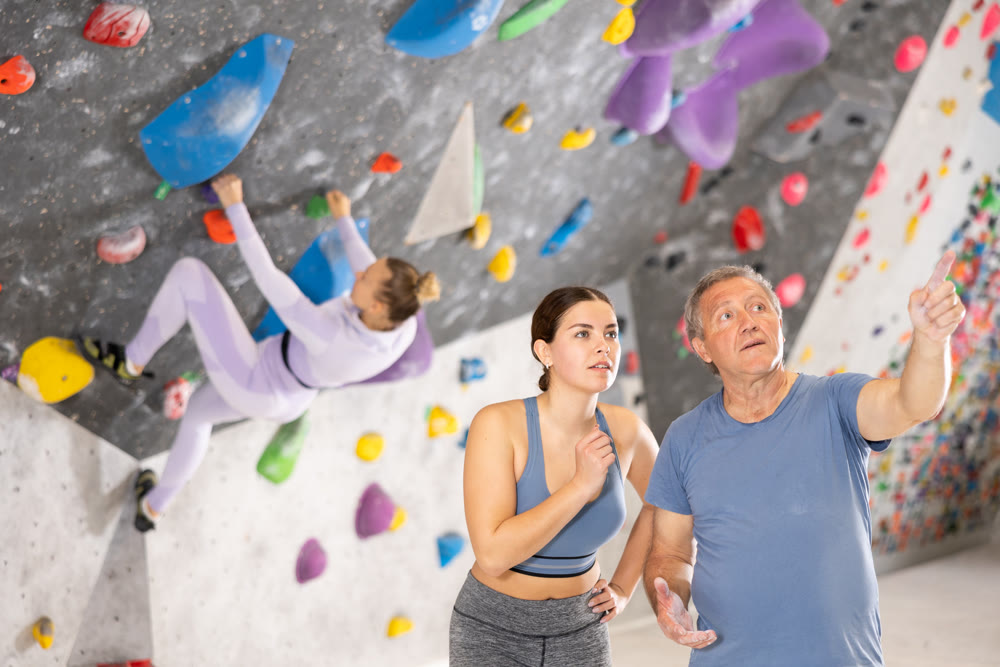 Trainer giving instructions to man on wall climbing at bouldering gym indoor