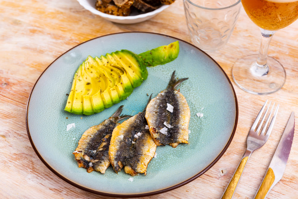 Smoked fillet of sardine carcass is served in plate with slices of ripe avocado.
