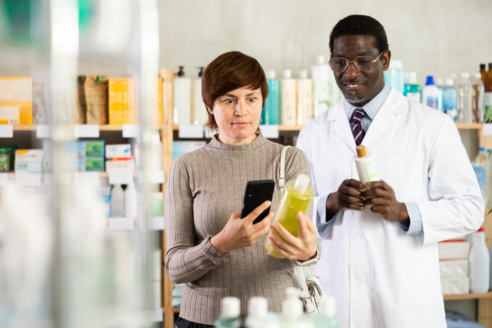 Woman in pharmacy scans QR code on antidandruff shampoo. African man pharmacist in background