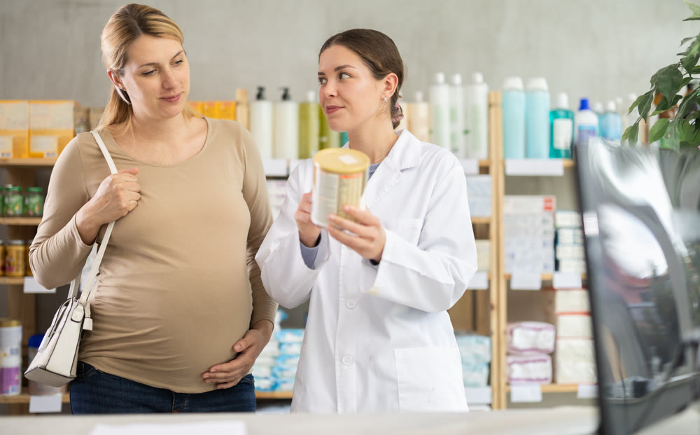 Smiling pharmacist offering newborn formula to expecting mother