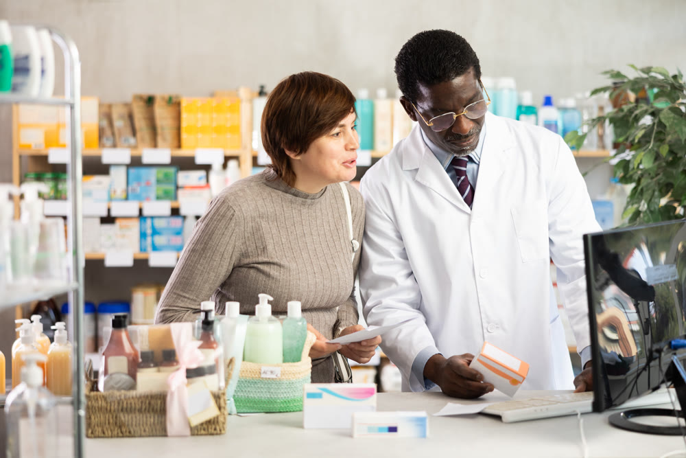 African man pharmacist uses computer at workplace and consulting woman client