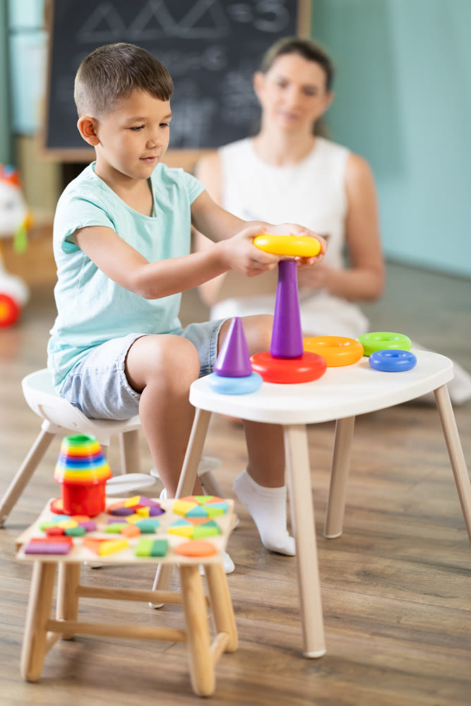 Boy builds a pyramid from children circles in kindergarten under supervision of child psychologist