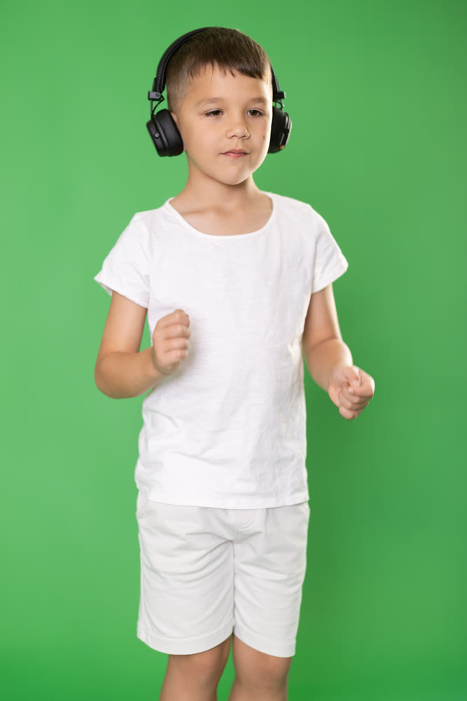 Boy in white t-shirt and shorts listens to music on headphones on green background