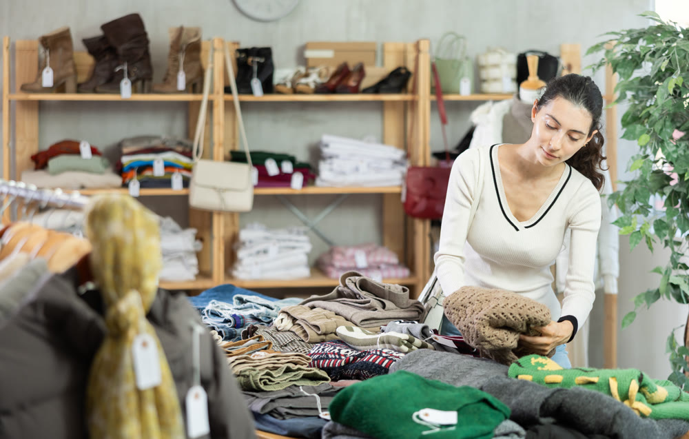 Woman carefully selects a warm sweater, pullover or cardigan in clothing store