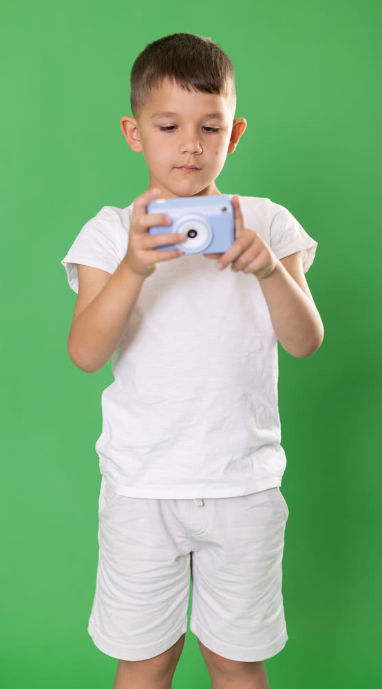 Boy in white t-shirt and shorts takes photo with camera against green background