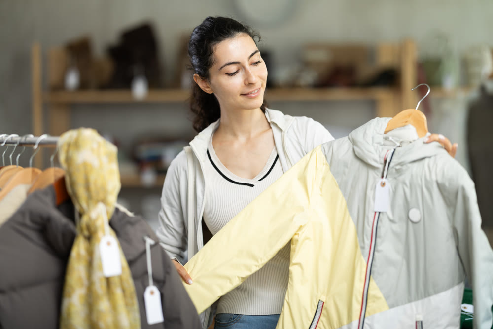 Female shopper chooses jacket in modern clothing store