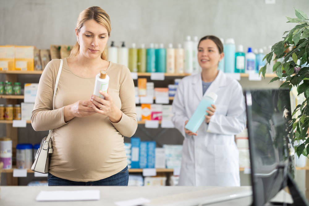 Pregnant woman choose shampoo in pharmacy, pharmacist in background offers similar product