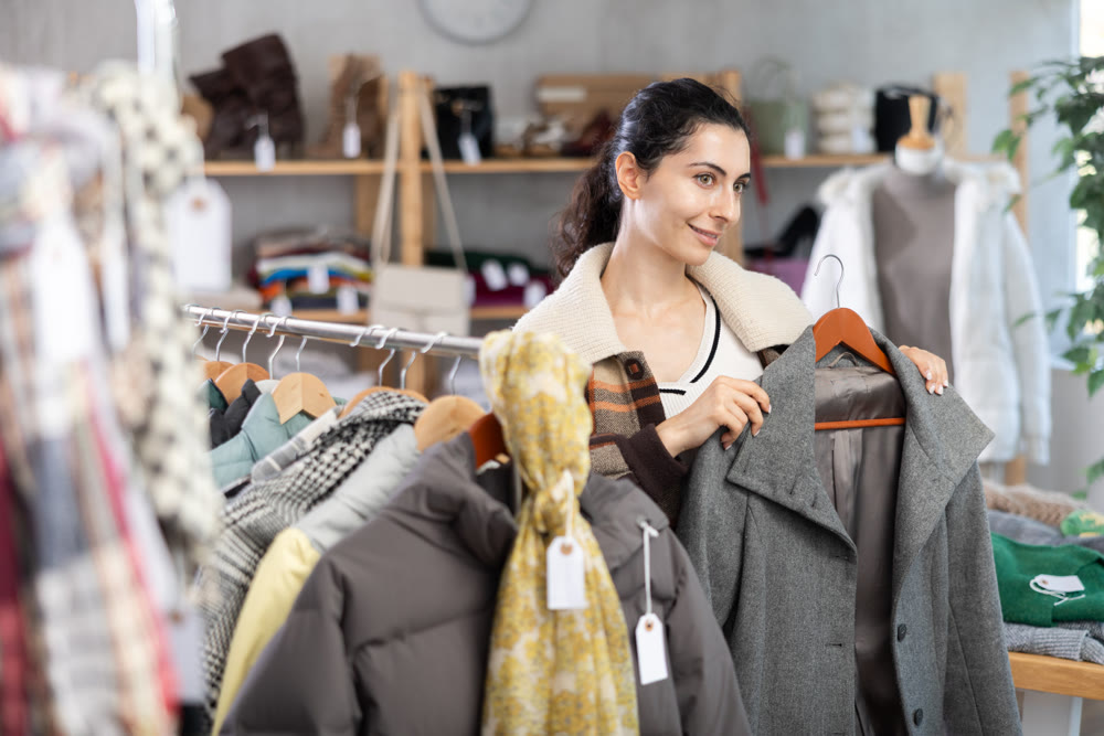 Armenian woman near showcase examine goods, buying drape coat.