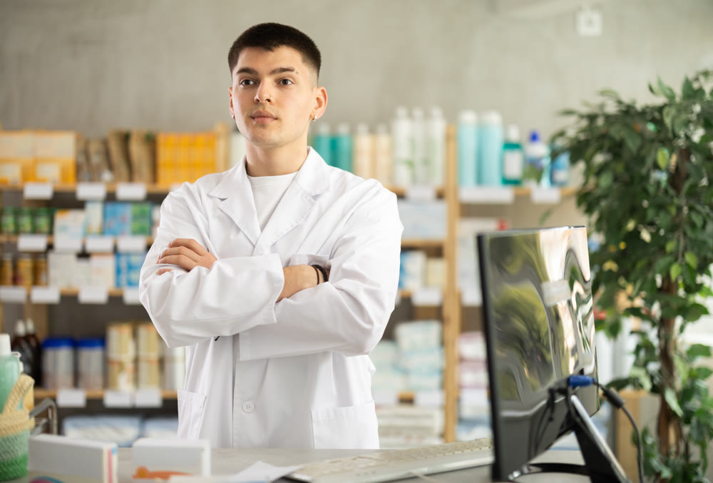 Guy pharmacist waits for visitors near cash register area with computer