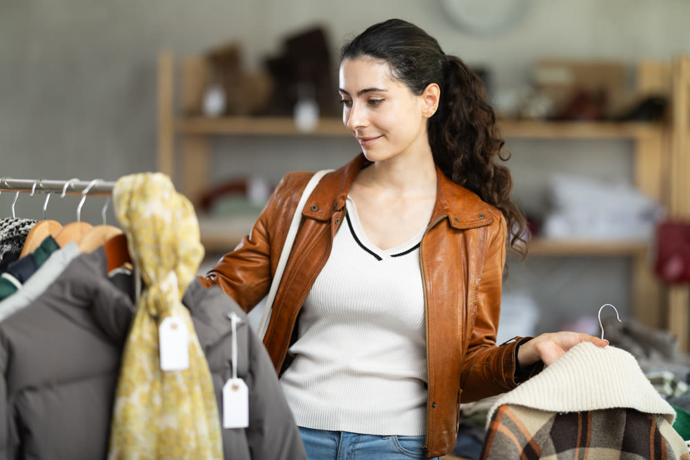 Female shopper chooses and try beautiful checkered coat-jacket in clothing store