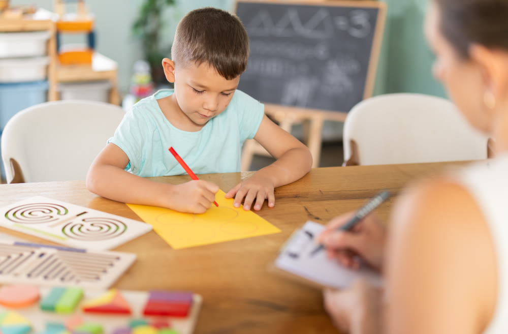 Little boy tracing figures on yellow sheet during psychological test