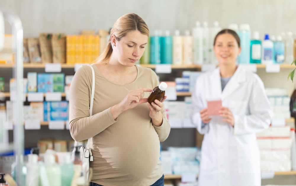 Pregnant woman choosing herbal syrup in local pharmacy