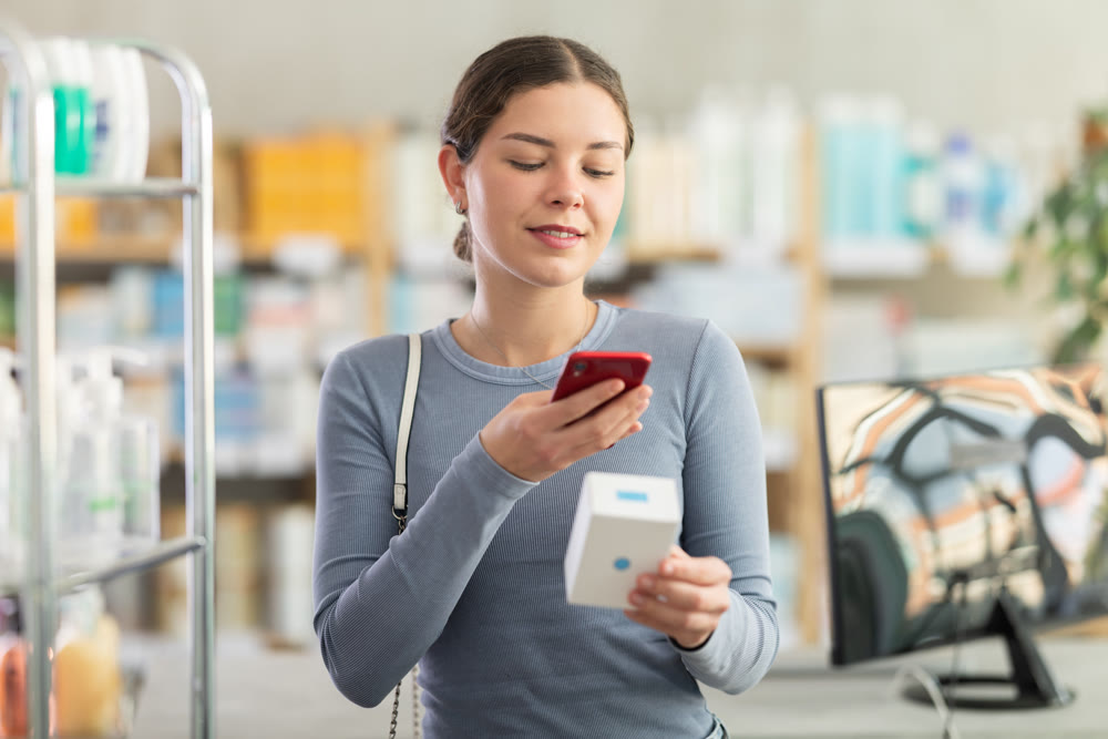 Woman scanning barcode on medicine box with phone at pharmacy