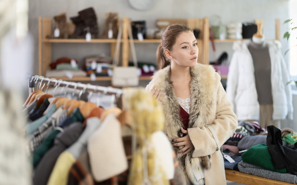 Girl try on fur coat in store and carefully examines her reflection in mirror