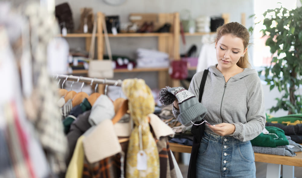 Young woman choosing a hat against the background of clothes hangers