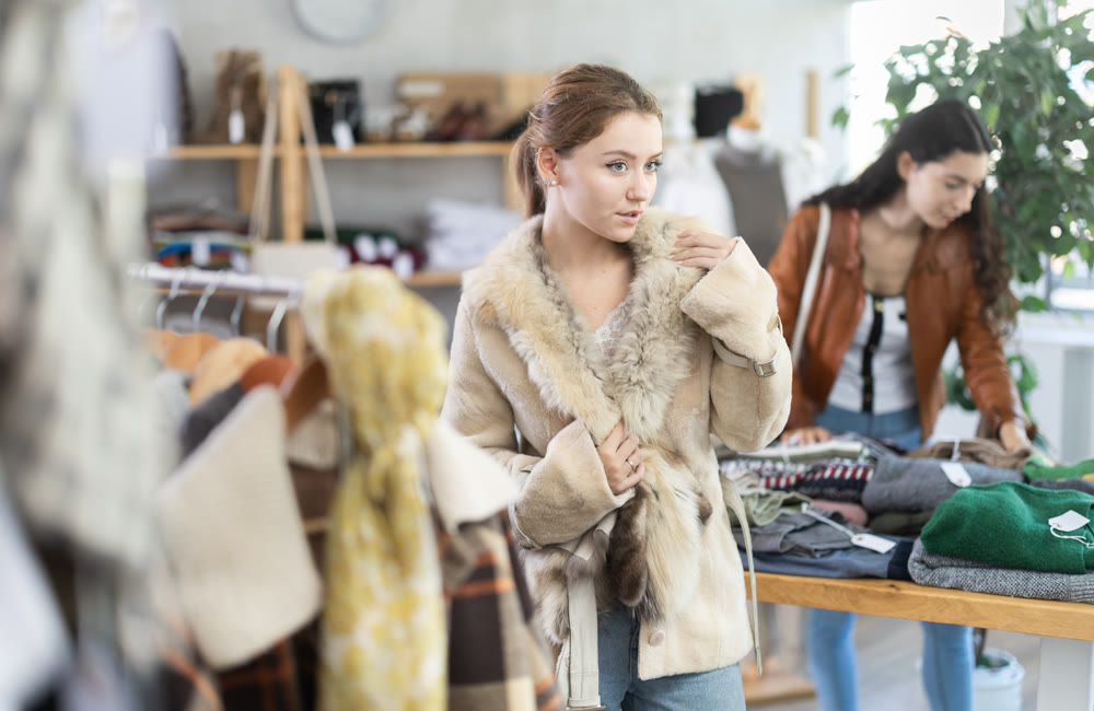 Girl try on fur coat in store and carefully examines her reflection in mirror