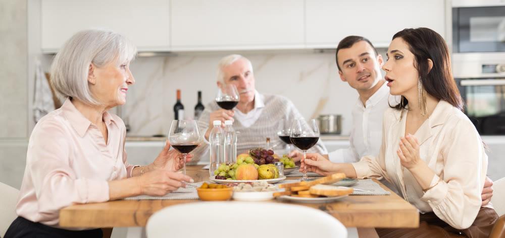Mature married couple are sitting at table, enjoying food and wine with middle-aged guests.