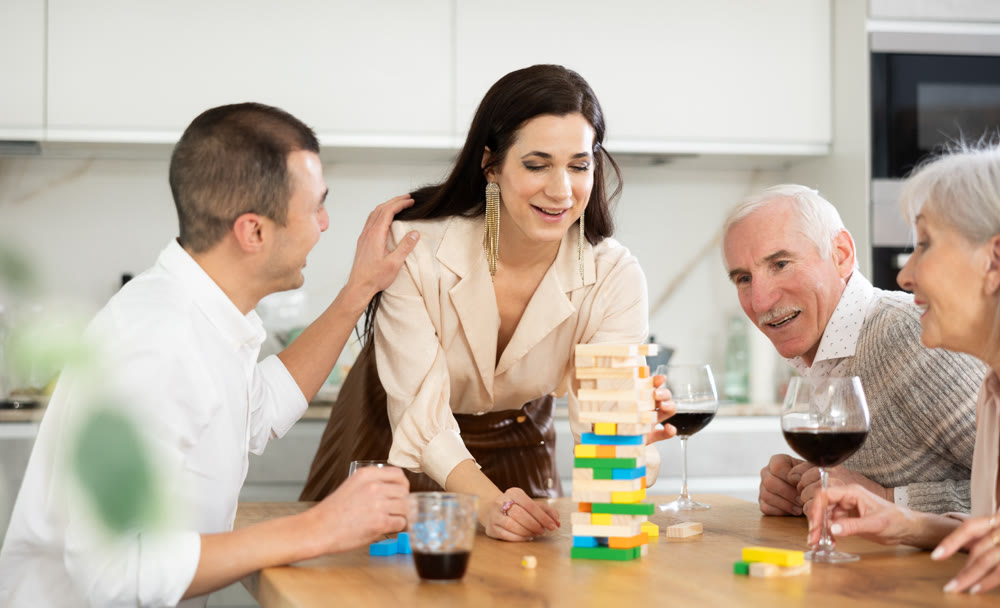Positive woman playing jenga with husband and senior parents-in-law