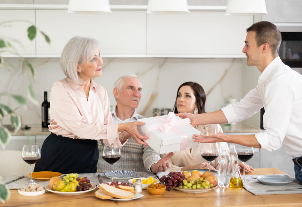 Man presenting gift to elderly mother of girlfriend at family meal