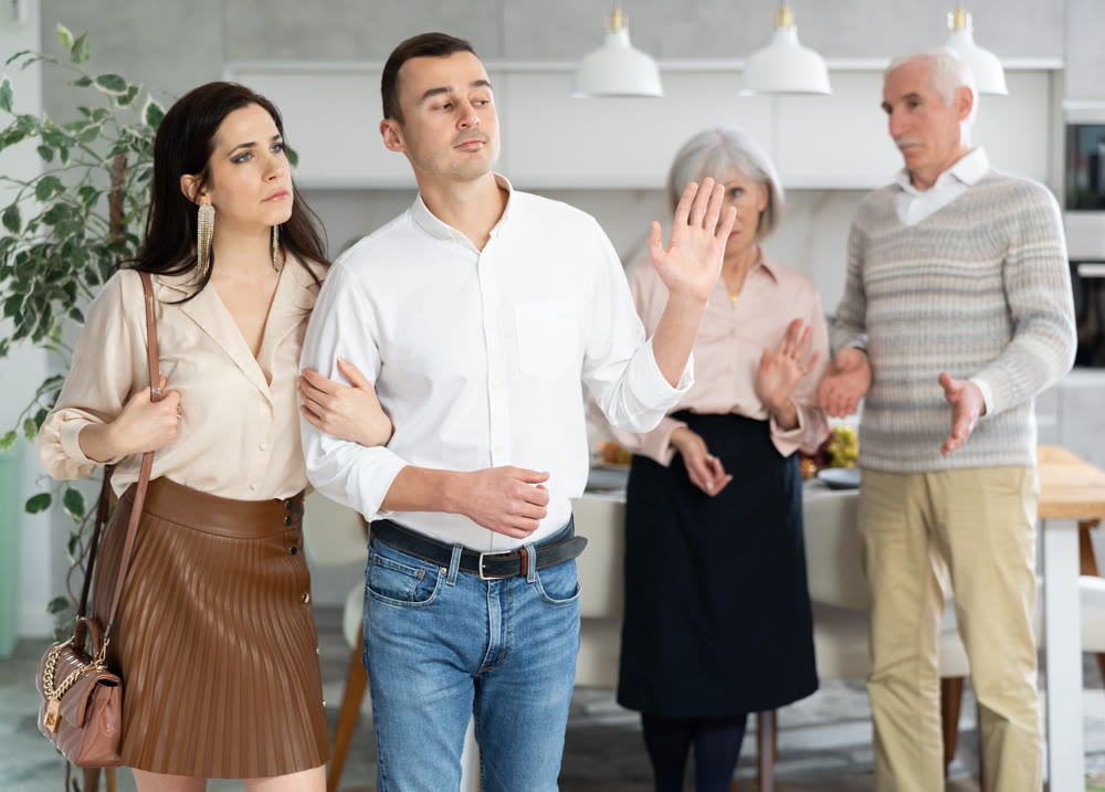 Sad young couple leaving the house while discontented senior parents standing behind
