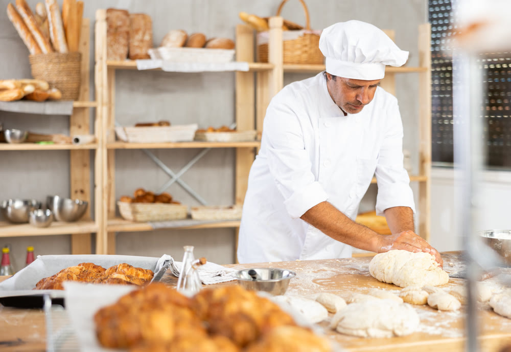 Adult male baker kneading dough on table