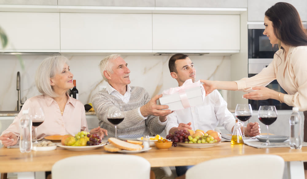 Birthday senior man accepts outright gift and greetings from adult daughter during family feast