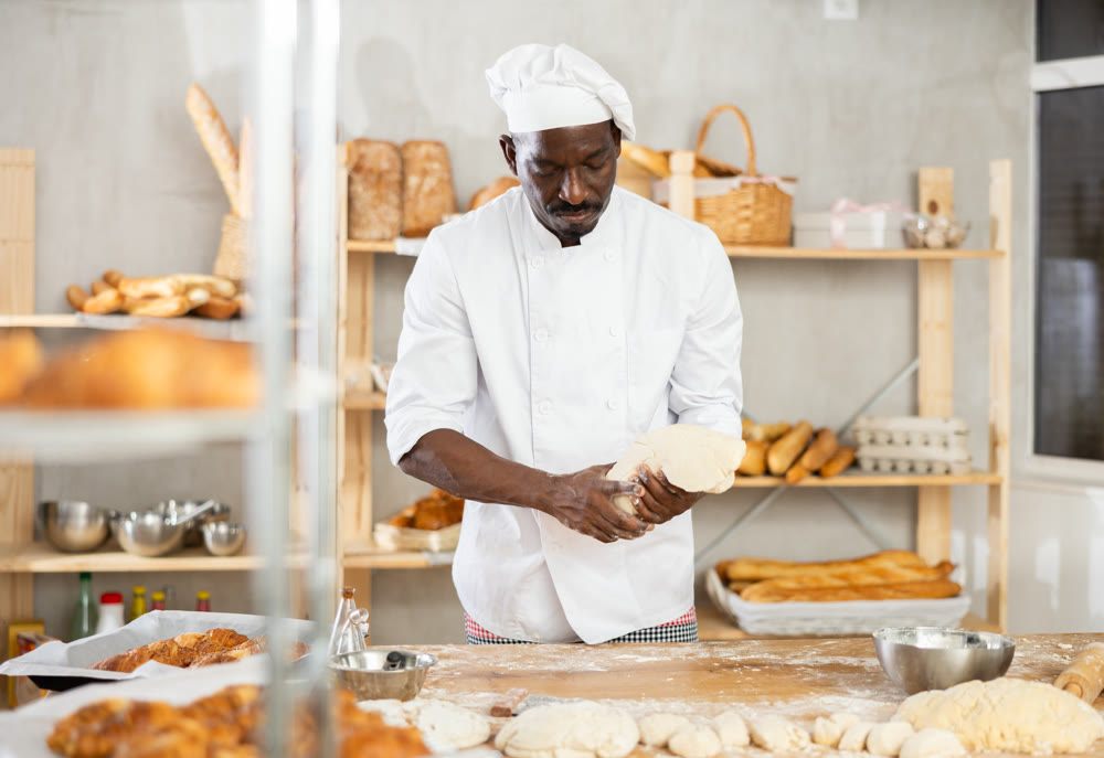 Experienced black baker kneading dough in artisan bakery