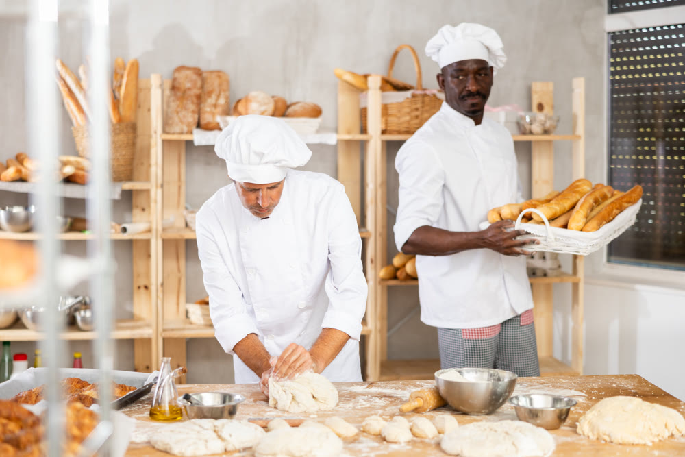 Caucasian guy works in bakery as baker, kneads dough, works with flour.