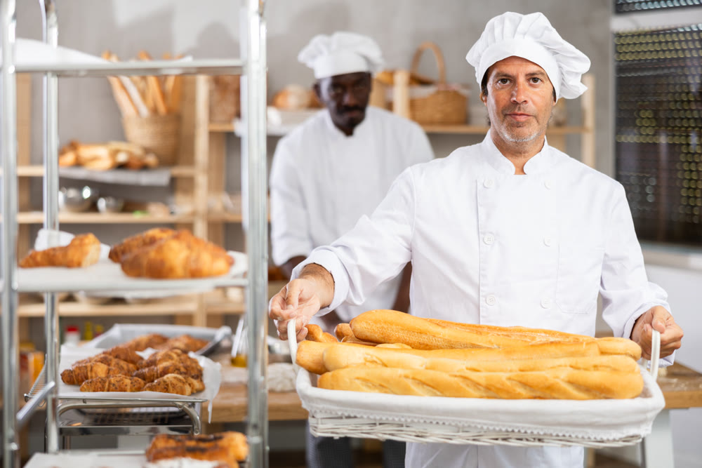 Successful baker proudly presenting freshly baked baguettes in cozy bakery