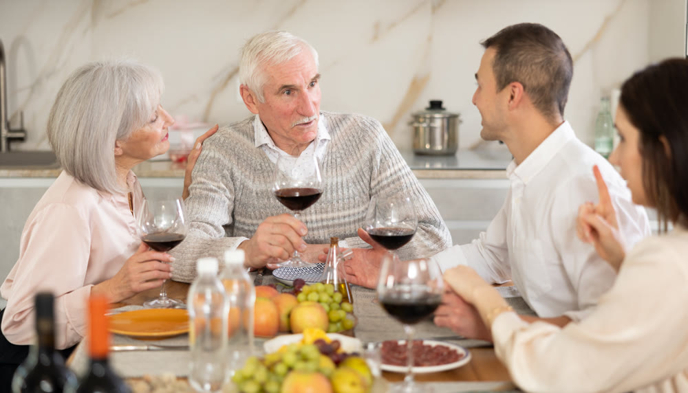 Senior parents and young couple sitting at table drinking wine and having conversation