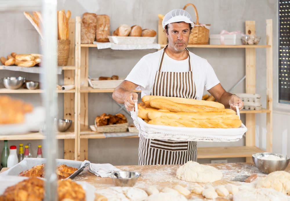 Portrait of baker holding tasty hot bread and baguettes in hands in kitchen