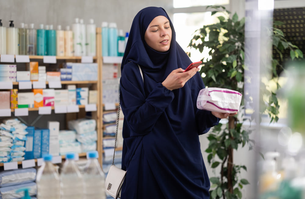 Young woman in hijab scanning qr code of feminine pads
