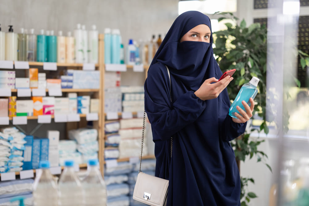Young woman in hijab scanning qr code of mouthwash