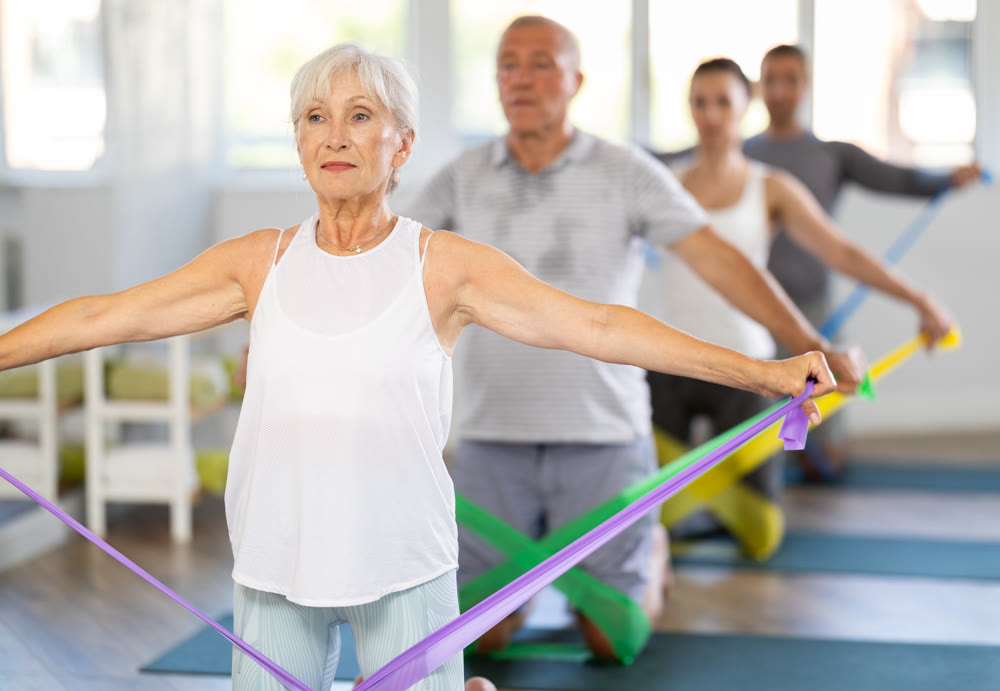 Elderly woman performs exercises with elastic band during Pilates strength training, kneeling