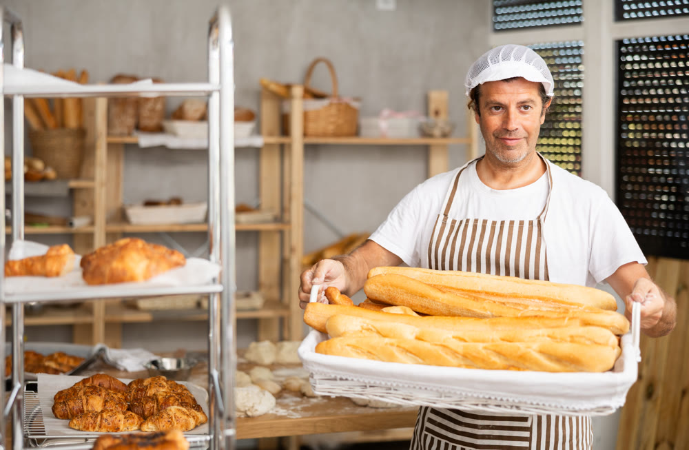 Caucasian male cook-baker worker with basket of baguettes, shows many products