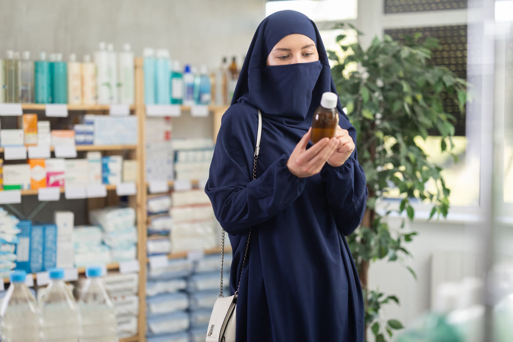 Young Muslim woman customer choosing syrup in drugstore