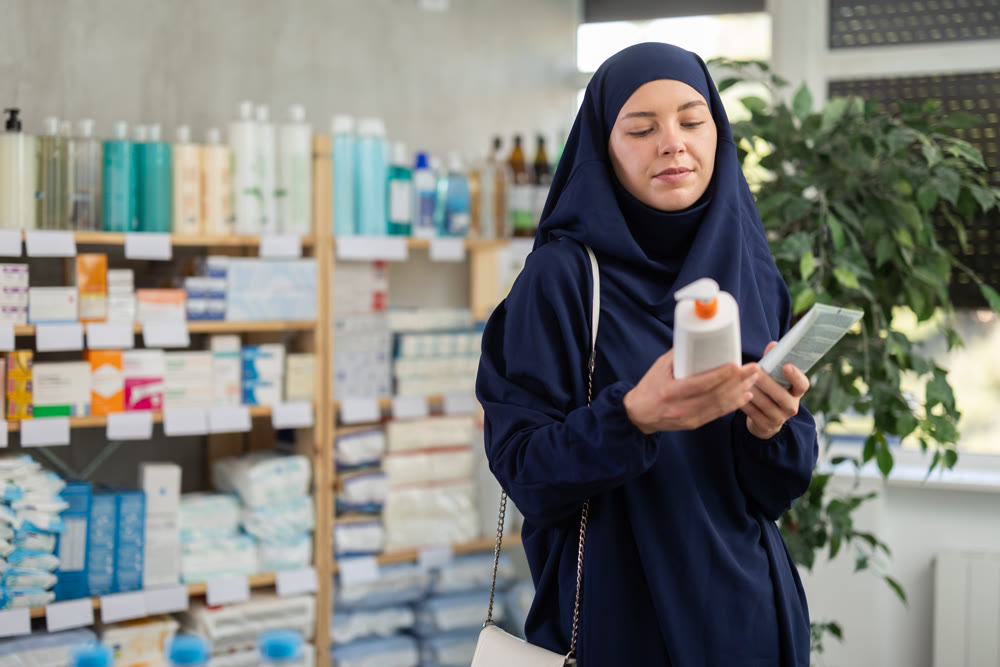 Young Muslim woman selecting body cream in pharmacy