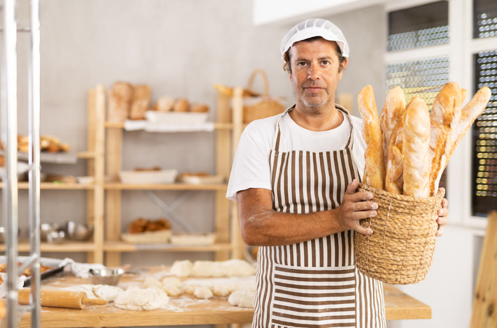 Caucasian male cook-baker worker with basket of baguettes, shows many products