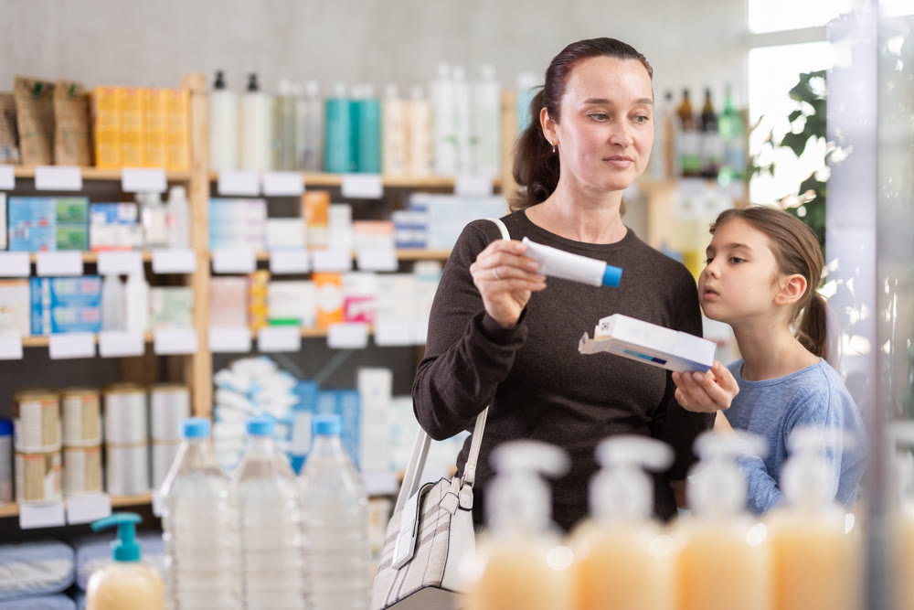 Woman with schoolgirl daughter are busy choosing ointment at pharmacy